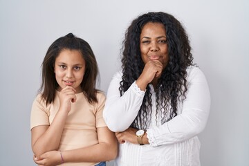 Poster - Mother and young daughter standing over white background with hand on chin thinking about question, pensive expression. smiling and thoughtful face. doubt concept.