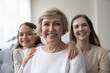 © fizkes - Attractive optimistic mature 60s woman looks at camera pose for picture with lovely granddaughter and young adult daughter. Caucasian female relatives feel happy, portrait of intergenerational family