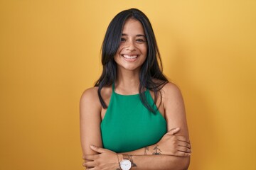 Poster - Brunette woman standing over yellow background happy face smiling with crossed arms looking at the camera. positive person.