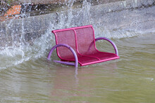 A Park Bench Is Flooded By High Water And Stands In The Water While The Waves Splash Over It