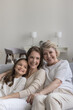© fizkes - Portrait of three pretty women, multi generational family, female dynasty hugging seated on sofa, laughing, enjoy pleasant pastime together at home, feel happy, enjoy harmonic relationships and bond
