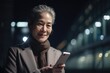 © InfiniteFlow - a senior chinese japanese businesswoman executive using mobile phone with background of modern office buildings at night Generative AI AIG18.