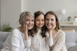 © fizkes - Portrait of happy cute little 6s girl posing for camera with retired elderly granny and young attractive mother sit together on couch smile looking at camera, showing care, feeling unconditional love