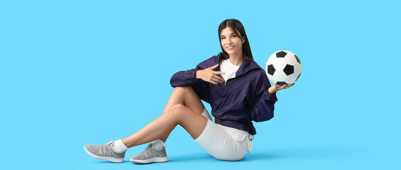 Young woman with soccer ball sitting against blue background