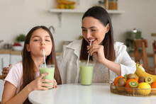 Little girl with her mother drinking green smoothie at table in kitchen