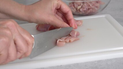 Wall Mural - The chef cuts raw chicken meat on a white plastic cutting board, close-up view, preparation process