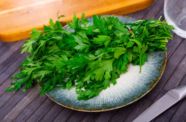 Wall Mural - Parsley sprigs on plate, on wooden table. Food ingredient, preparing food concept.