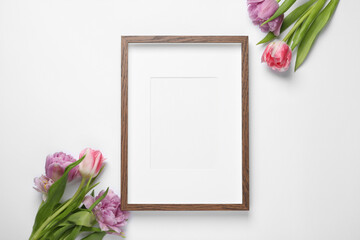 Wall Mural - Empty photo frame and beautiful tulip flowers on white background, flat lay. Space for design