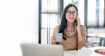 Young happy asian woman talking on mobile phone, relaxing while working at co-workspace.