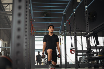 Strong Asian man doing lunge exercise with kettlebell at cross fit gym. Athlete male wearing sportswear workout on grey gym background with weight and dumbbell equipment. Healthy lifestyle.
