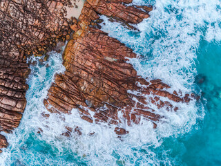 Wall Mural - Aerial top down view of rocks and clear blue water. Ocean waves smashing on the rocks as a background. Beautiful natural winter vacation holidays background. Margaret River, Western Australia. Coastal