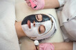 © RomanR - The cosmetologist applies a black and white mask on half of the face at spa salon