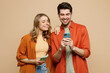 © ViDi Studio - Young smiling happy couple two friends family man woman wear casual clothes hold in hand use mobile cell phone together chatting isolated on pastel plain light beige color background studio portrait.