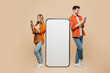 © ViDi Studio - Full body happy young couple two friends family man woman wear casual clothes together big huge blank screen mobile cell phone with area use smartphone isolated on pastel plain light beige background.