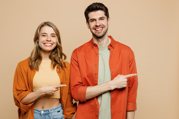 Wall Mural - Young cheerful happy fun couple two friend family man woman wear casual clothes point index finger aside on area mock up together isolated on pastel plain light beige color background studio portrait