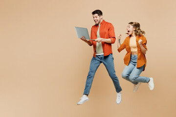 Full body young couple two friends family IT man woman wear casual clothes together hold use work on laptop pc computer do winner gesture isolated on pastel plain light beige color background studio.