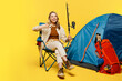 Full body young woman sit near bag with stuff tent hold fishing rod show thumb up isolated on plain yellow background. Tourist active lifestyle walk on spare time Hiking trek rest travel trip concept