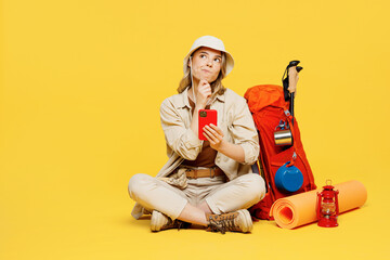 Full body young woman carry bag with stuff mat sit using mobile cell phone isolated on plain yellow background. Tourist leads active lifestyle walk on spare time. Hiking trek rest travel trip concept.