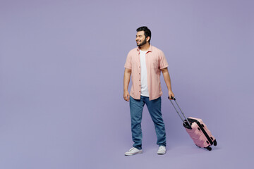 Traveler Indian man wearing casual clothes shirt hold suitcase walk going isolated on plain purple background. Tourist travel abroad in free spare time rest getaway. Air flight trip journey concept.