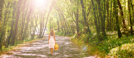 Wall Mural - Woman wearing white dress walking in forest with sunlight