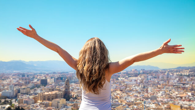 Happy free woman with arms up admiring skyling of Malaga city- City skyline with arms outstretched raised in the sky- success,  travel,  active life concept