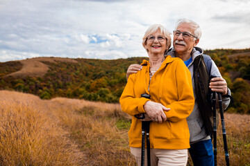 portrait of active senior couple with backpacks hiking together in nature on autumn day.