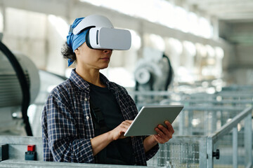 Wall Mural - Female engineer connecting tablet pc with VR glasses and using them in her work in factory