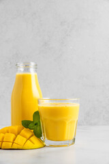 Wall Mural - Mango smoothie in bottle and glass. Summer tropical drink on white background with copy space