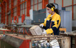 © Nassorn - Female industrial engineer in white helmet, safety jacket and headphone work in heavy metal engineering factory. Latin technician woman inspecting production line in metalwork warehouse facility.