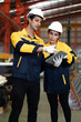 © Nassorn - Hispanic industrial engineers in white helmet and safety jacket work in heavy metal engineering factory. Latin technician workers using tablet computer in metalwork manufacturing facility, portrait.