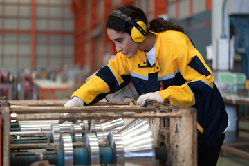 Wall Mural - Female industrial engineer in white helmet, safety jacket and headphone work in heavy metal engineering factory. Latin technician woman inspecting production line in metalwork warehouse facility.