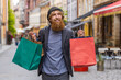 © Andrii Iemelianenko - Happy smiling young adult man shopaholic consumer after shopping sale with full bags with gifts outdoors. Redhead bearded guy tourist traveler walking along the urban city street road. Town lifestyles