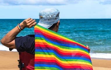 Disabled woman holding LGBTQ rainbow flag in front of sea, LGBT and pride month Concept