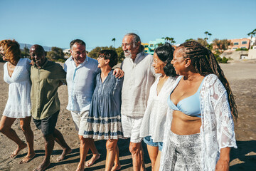 Wall Mural - Happy senior people having fun walking on the beach at sunset wearing summer clothes - Joyful elderly lifestyle, vacation and travel concept - Main focus on center friends faces
