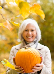 Canvas Print - Older woman holding pumpkin in park