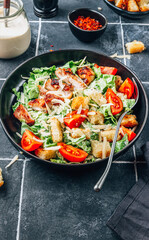 Wall Mural - Homemade Caesar salad with crispy chicken and tomatoes on a black tiled background