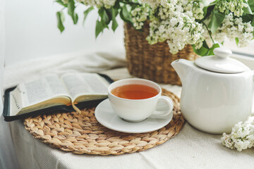 A cup of tea, a basket of lilacs and an open Bible