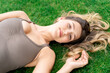 © pavelgulea - Young slim fit woman with loose long blond healthy hair and make up in fitness clothes lying on green grass loan relaxing after training, workout or running on summer weekend. Leisure activity