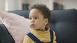 © Synthex - Sweet African American child with natural black hair sitting on sofa and looking around