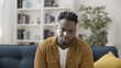 © Synthex - Upset African American man sitting on sofa, problems of unemployment and financial debt