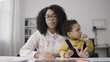 © Synthex - African American single mother holding her baby on her lap while having a work call online
