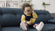 © Synthex - Cute small baby boy in big eyeglasses plays on his smartphone while sitting on the sofa