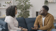 © Synthex - African American man talking with his wife on sofa, relationship crisis