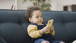© Synthex - Cute African American toddler holding smartphone, looking at screen, smiling