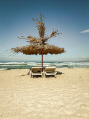 Straw parasol and two lounge chairs on a beach in retro look.