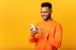 © Vadim Pastuh - Ecstatic young Indian man standing isolated on yellow and using trendy smartphone, looking at screen and smiling joyfully, millennial guy enjoy new mobile application features