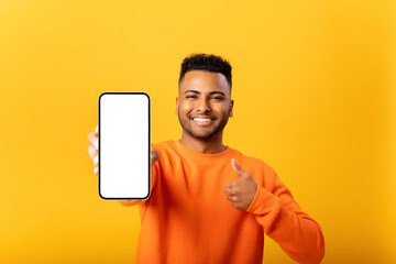 Portrait of handsome young man demonstrates smartphone with blank screen and shows thumb up, guy likes mobile app, looking and smiling at the camera, feels satisfied, isolated