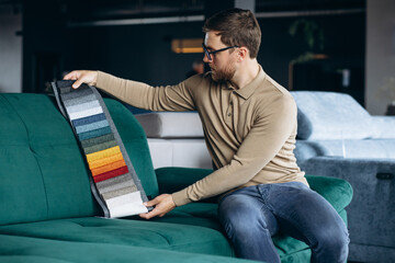 Man sitting on sofa in furniture store choosing textile