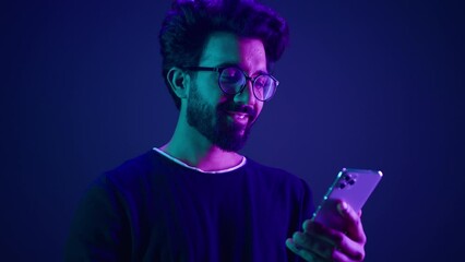 Arabian male using mobile phone chatting browsing smartphone online order shopping gaming with cellphone Indian man scrolling social media internet technology app at neon ultraviolet studio background