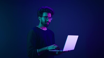 Arabian man with laptop at neon ultraviolet background Indian guy male coder programmer worker user with computer coding modern technology showing thumb up recommend online service approve good app